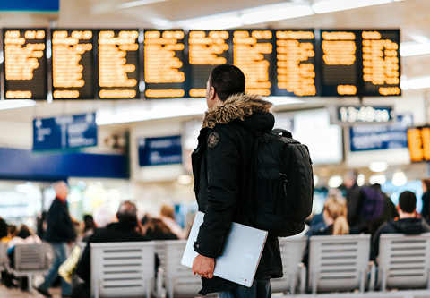 Studente in una stazione dei treni che guarda il tabellone degli orari